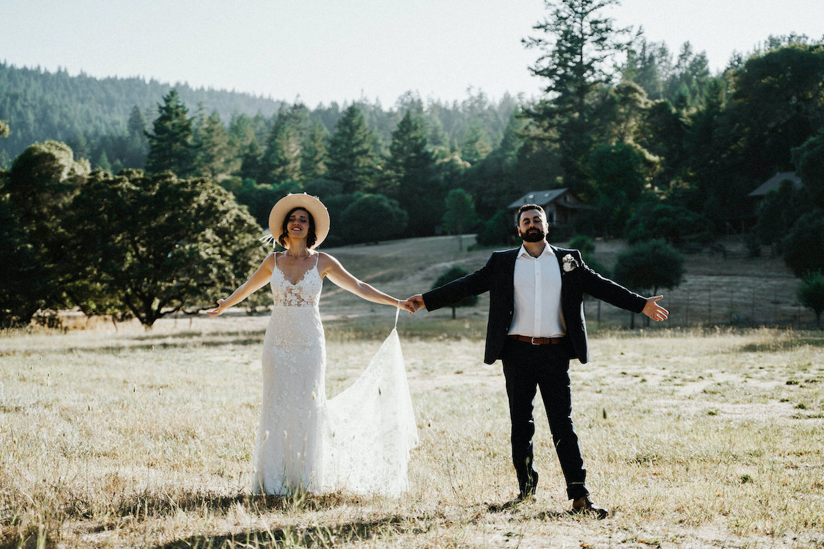 Newlyweds holding hands with arms outstretched in an open field