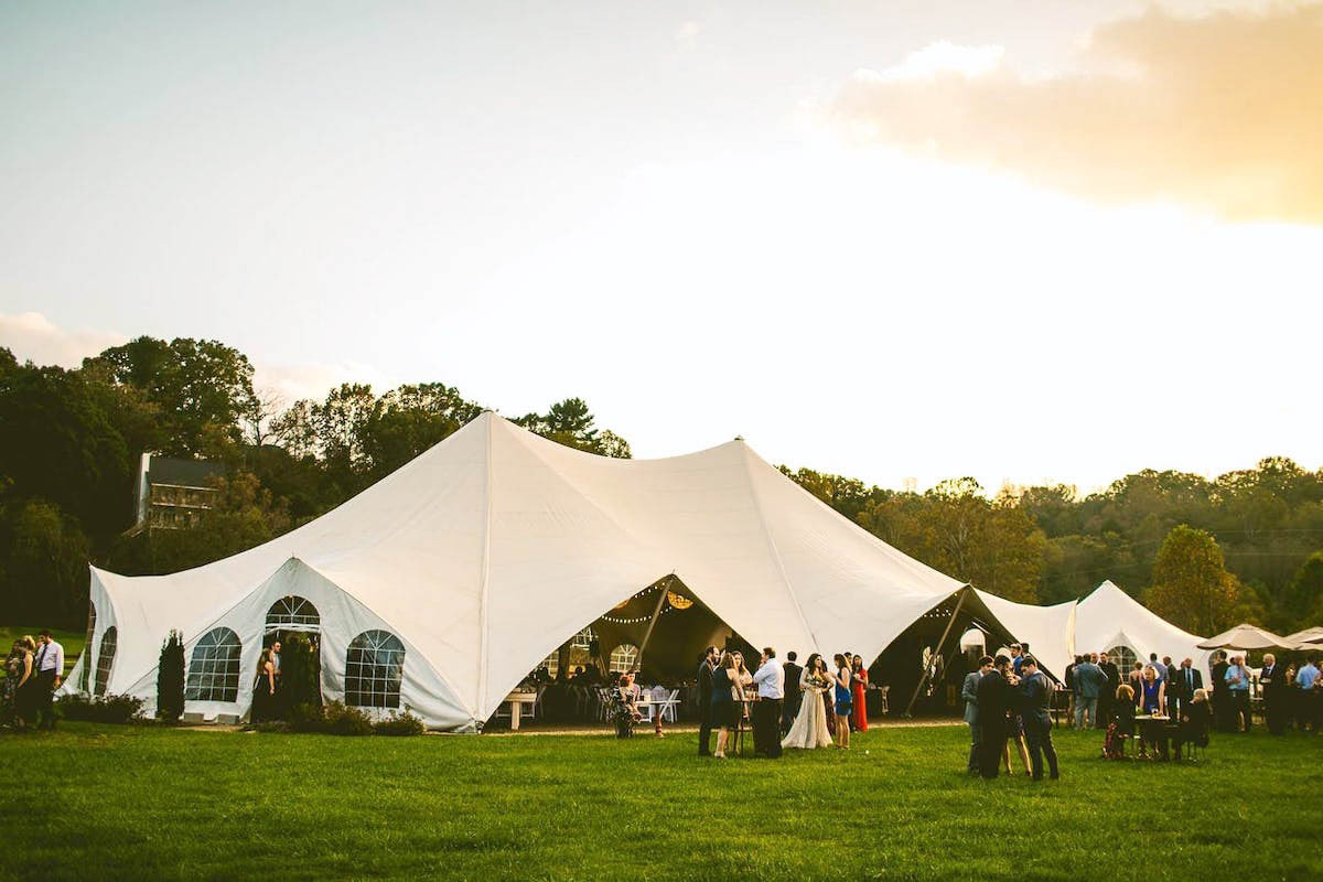 A large white tented wedding reception on a sprawling green lawn
