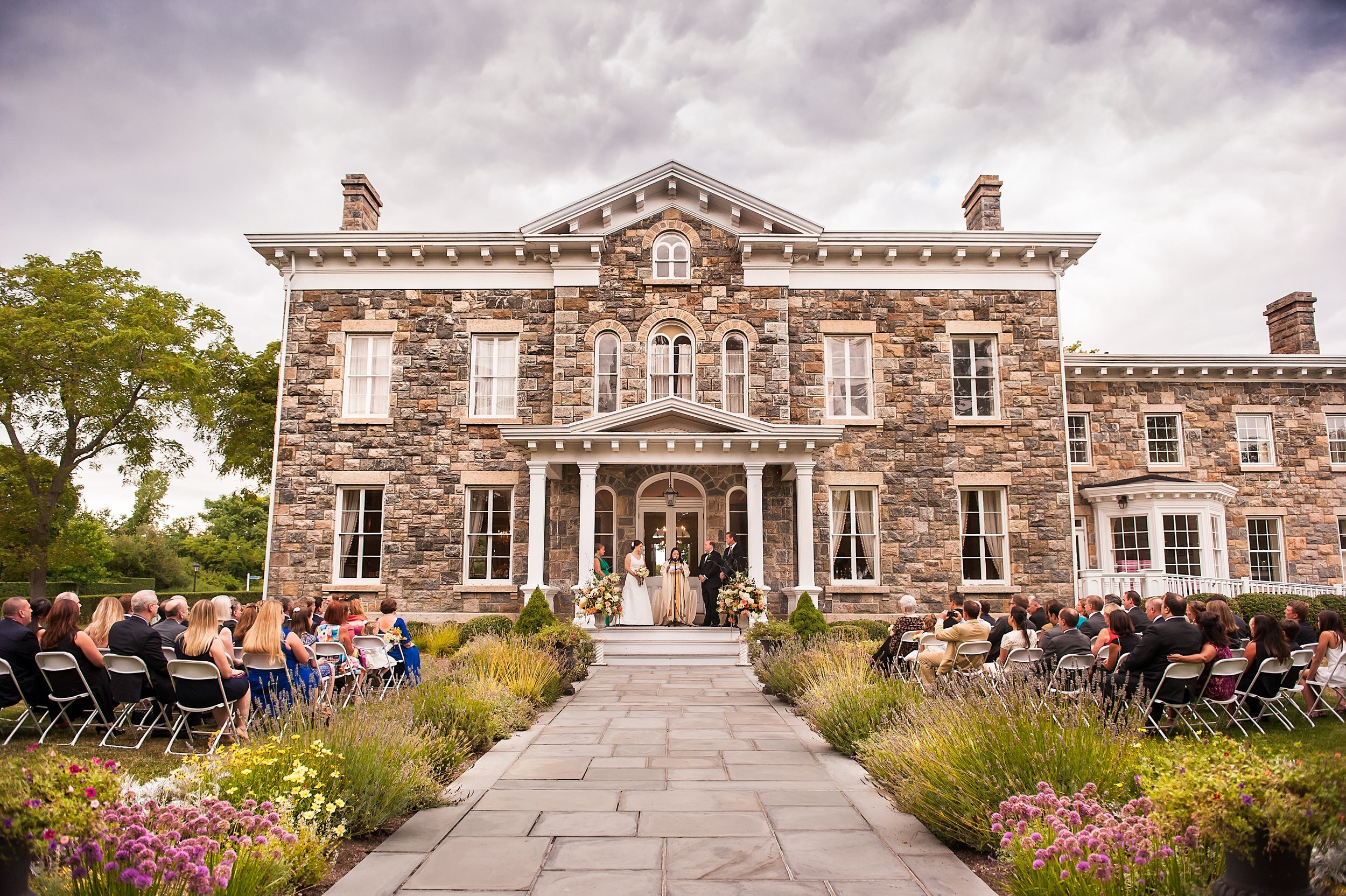 Outdoor wedding ceremony in front of a large stone mansion.