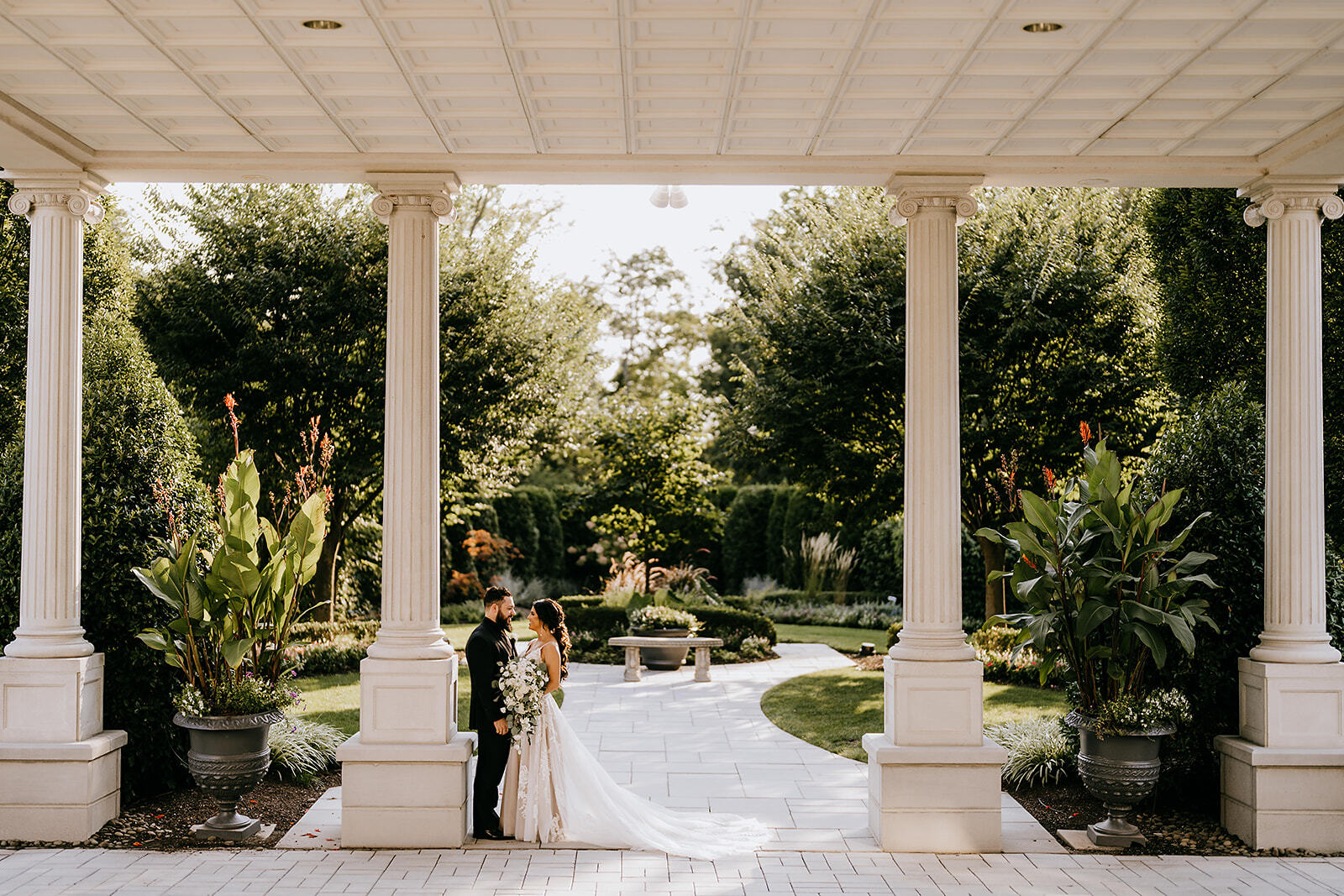 Bride and groom posing beneath white columns in a formal garden
