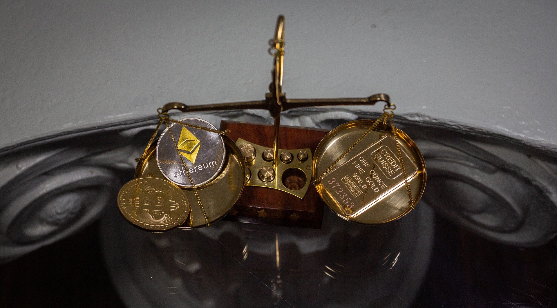 A scale weighing Bitcoin and Ethereum cryptocurrencies against a bar of gold