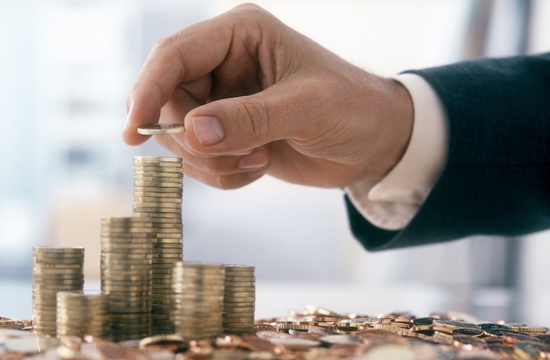 Stack of gold coins with hand holding one coin