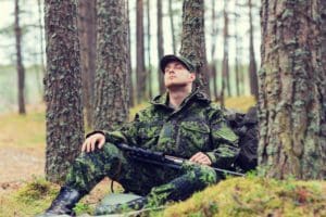 hunting, war, army and people concept - young soldier, ranger or hunter with gun sitting and sleeping in forest