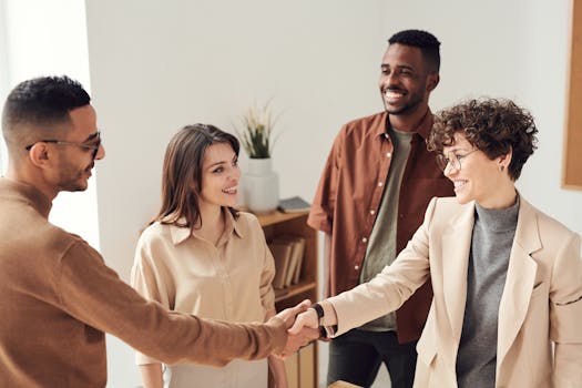 Four colleagues smiling and shaking hands in a bright office setting. trade show closing strategy
