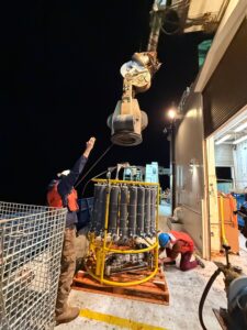 A CTD package composed of a round open frame with 24 vertical bottles for sampling of ocean water is readied for deployment.