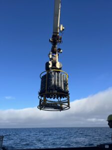 A CTD deployed over the ocean off the side of the Revelle on a blue-skied day.