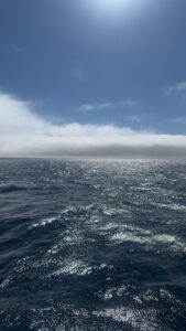 Dark, shiny seas are met on the horizon by clouds overlain by beautiful blue skies.