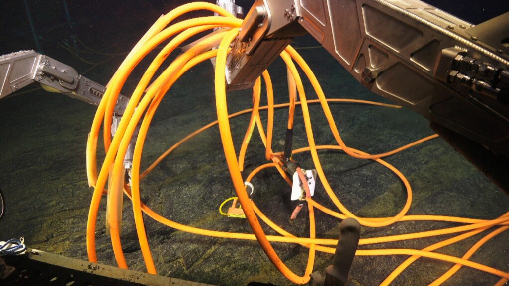 Robotic arms with loops of orange cable draped over them.