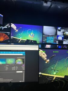 Four screens with various views. On one a robotic arm holds a knife