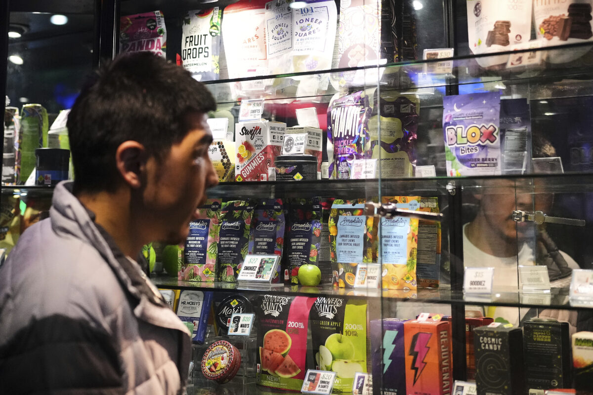 A man looks at a glass shelf with dozens of brightly colored cannabis products on display.