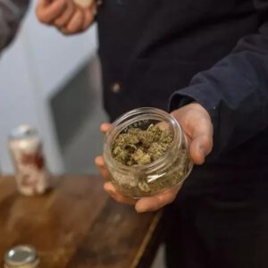 Man holds open jar of weed
