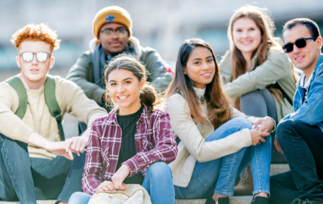 A group of smiling teens poses outdoors for a photo