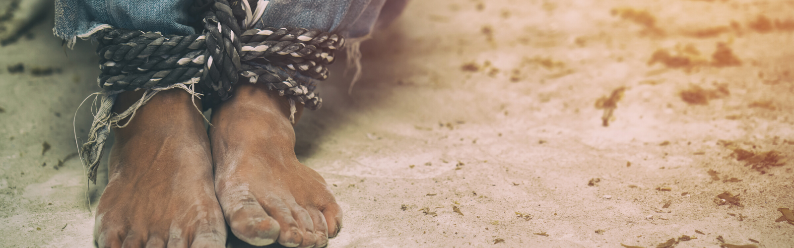 Child's bare feet in sand with rope tied around his legs to symbolize human trafficking.