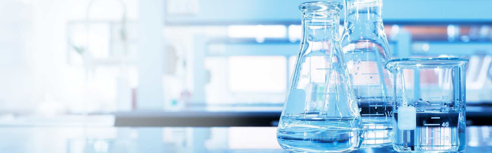 Laboratory table top with two Erlenmeyer flasks and a beaker reflecting a blue light.