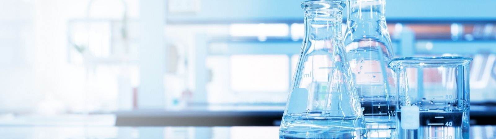 Laboratory table top with two Erlenmeyer flasks and a beaker reflecting a blue light.