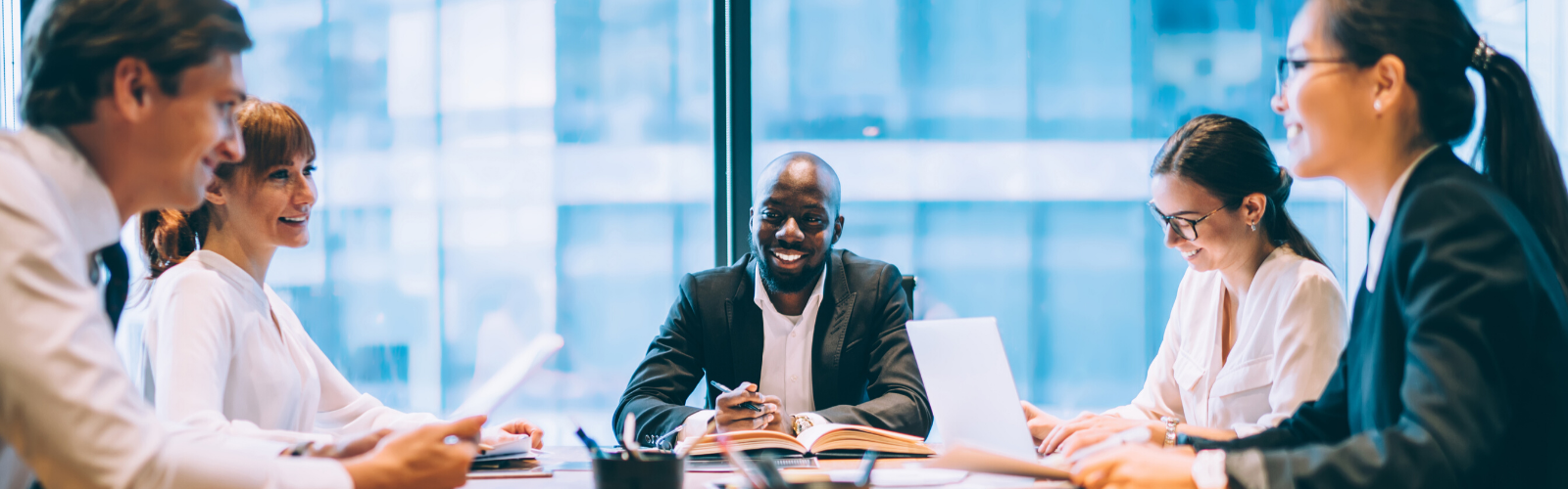 Happy professionals sitting around a table in a room smiling and having a great collaborative meeting.