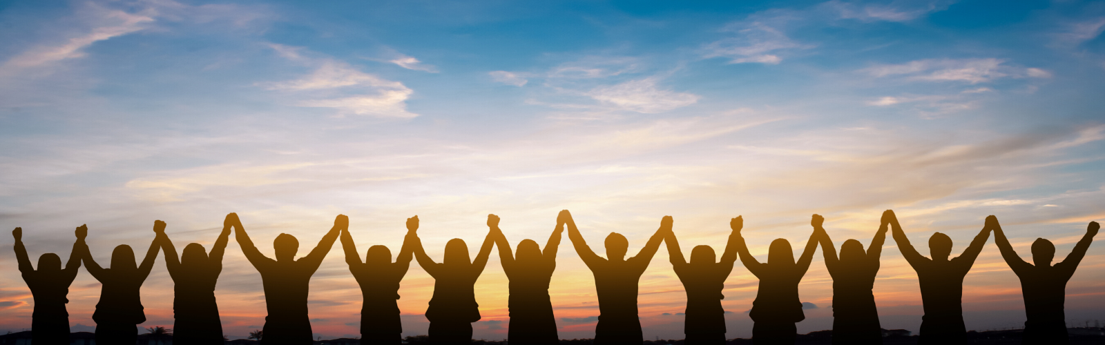 Professionals holding hands above heads in a triumphant, collaborative way facing a beautiful sunset to symbolize ethical, successful business practices.