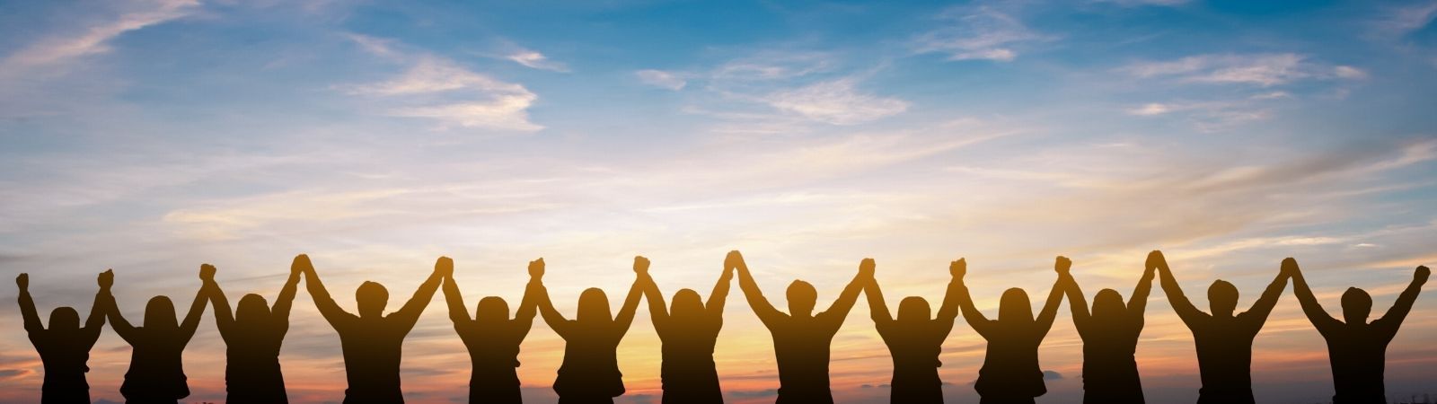 Professionals holding hands above heads in a triumphant, collaborative way facing a beautiful sunset to symbolize ethical, successful business practices.