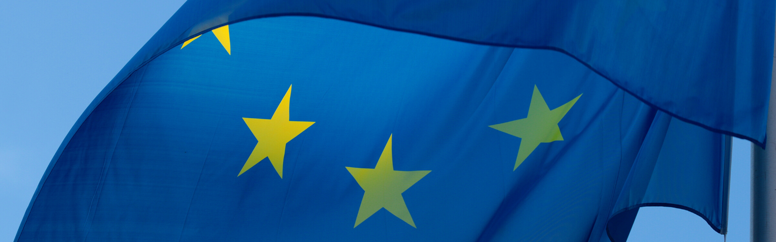 Close up of the EU flag waving in the wind against a bright blue, cloudless sky.