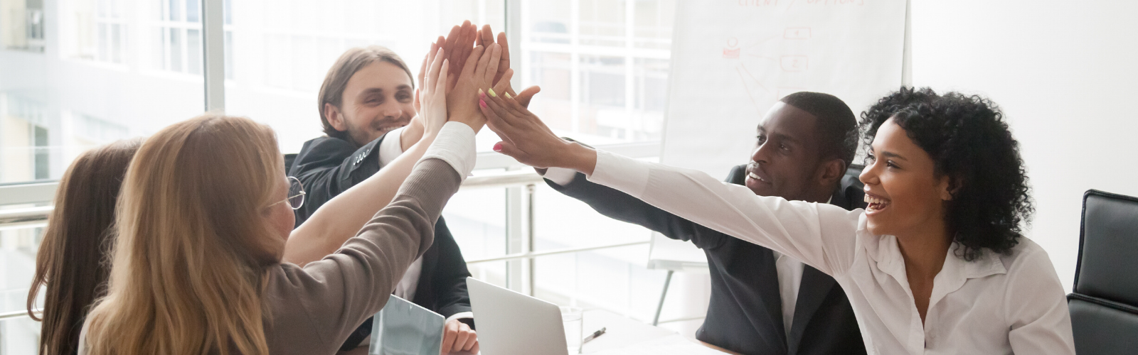 Happy business meeting with five smiling, diverse professionals high-fiving signifying collaboration.