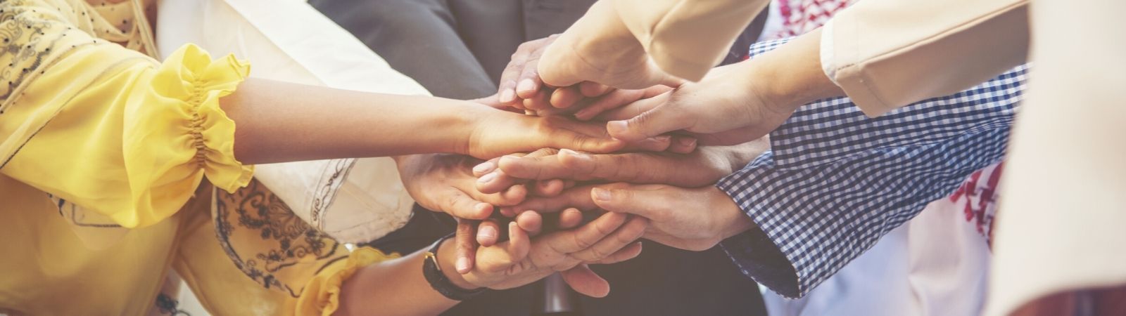 Diverse professionals from around the globe putting hands in the middle of a huddle to symbolize working together and supplier diversity.
