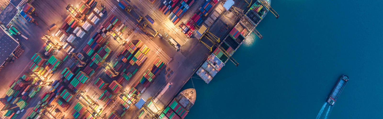 Ariel view of a shipping port with boats in dark blue water and colorful shipping containers on the port side, symbolizing international trade through the USMCA and NAFTA.
