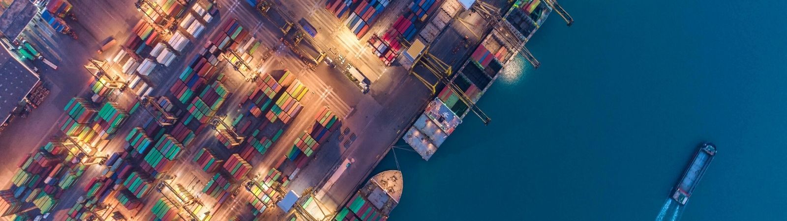 Ariel view of a shipping port with boats in dark blue water and colorful shipping containers on the port side, symbolizing international trade through the USMCA and NAFTA.