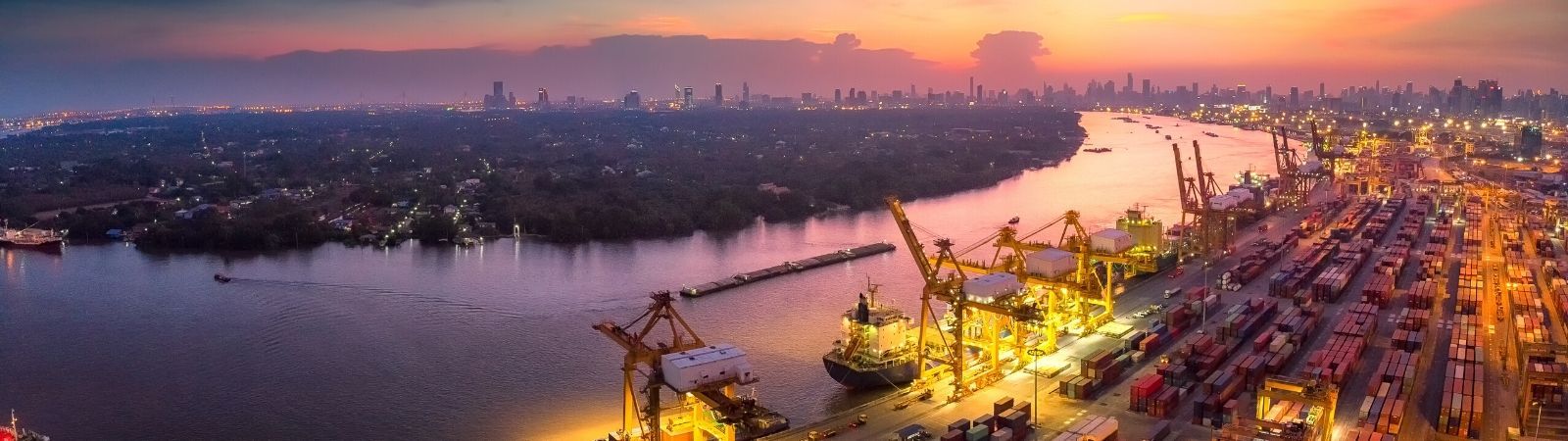 Panoramic view of a shipping port at night with cranes lit up by lights on the dock and shipping containers.