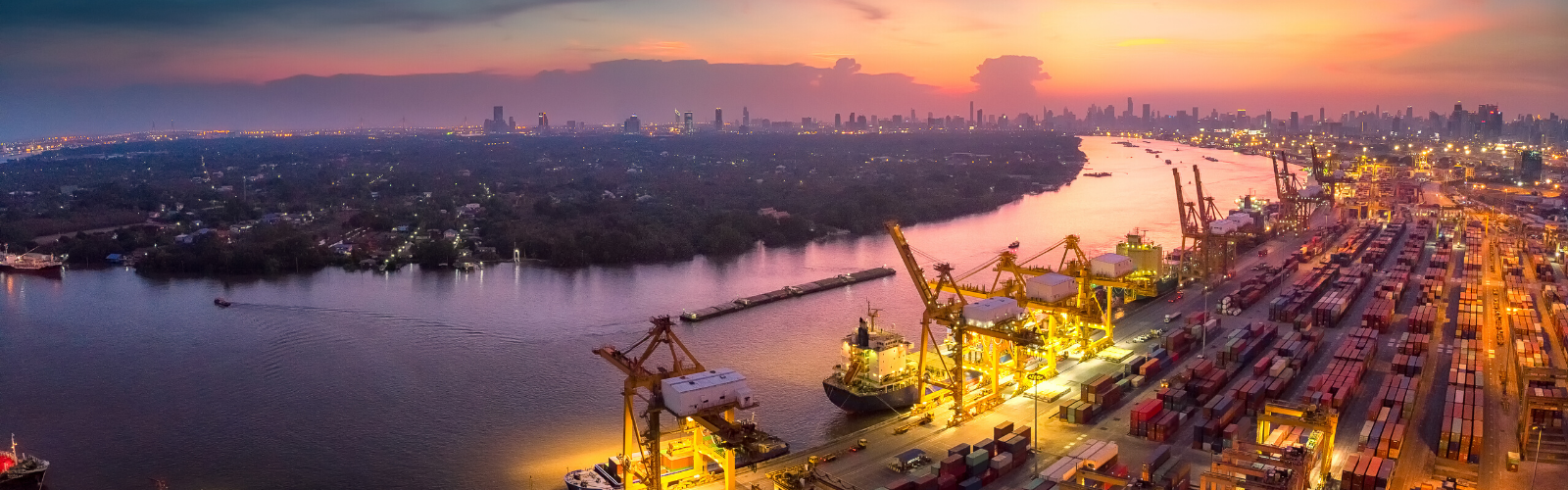 Panoramic view of a shipping port at night with cranes lit up by lights on the dock and shipping containers.