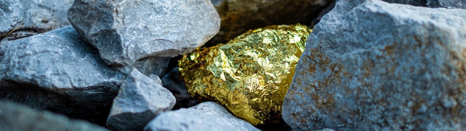 A gold nugget nestled and almost hidden in grey stones in a conflict minerals mine.