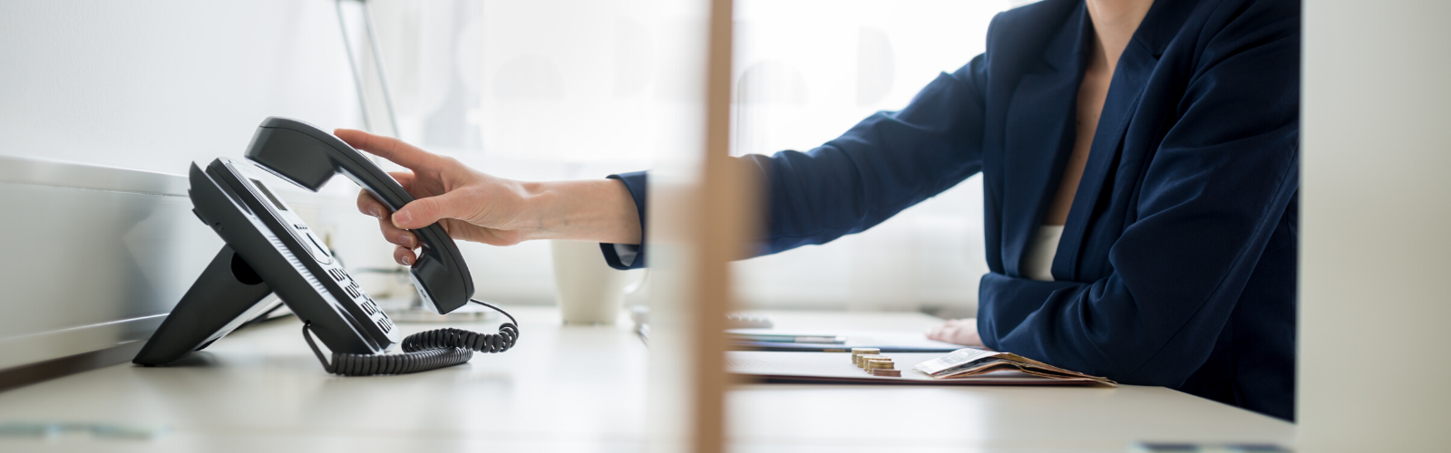 Professional woman at her desk picking up a landline office phone to call a whistleblower hotline.