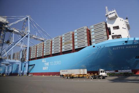A large blue container ship full of shipping containers with vehicles in front. 
