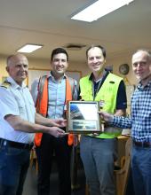 the vessel captains and port team stand holding a welcoming plaque
