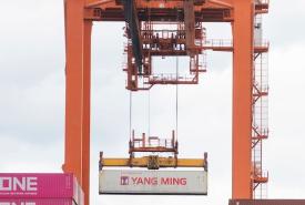A shot of an orange crane lifting a container with the words "Yang Ming" from a vessel. 