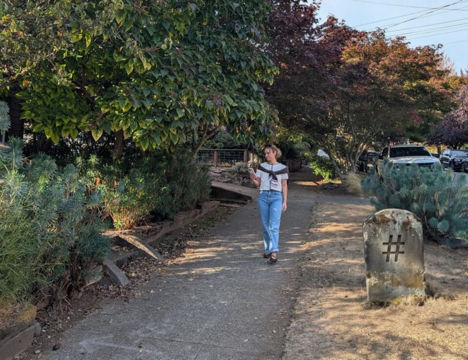A woman walks down a sidewalk past trees and a stone marker engraved with a hashtag symbol, a reminder of whether hashtags are still relevant.