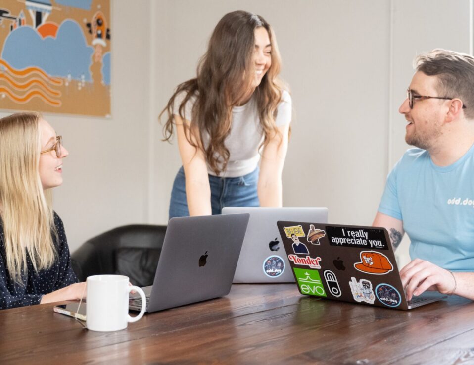 Three coworkers talking around a wooden table with laptops.