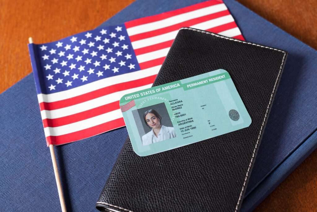 permanent resident green card on top of a desk with a wallet and American flag underneath
