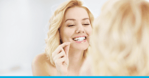Young woman flossing her teeth in the mirror