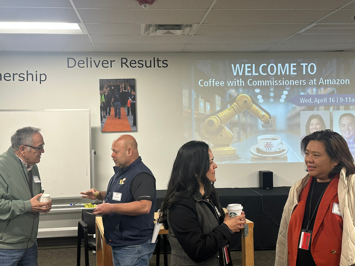 Two women talk while two men also talk behind them in an office. 