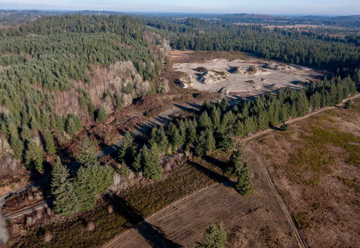 An aerial shot of a plot of land overlooking evergreen trees and a gravel mine.