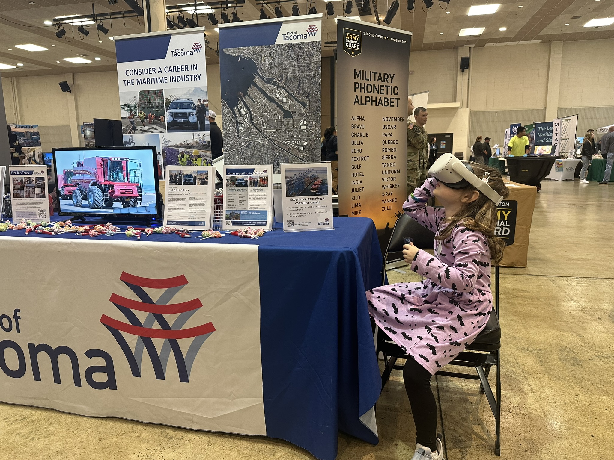 A girl in a dress sits at a booth wearing a VR headset. 