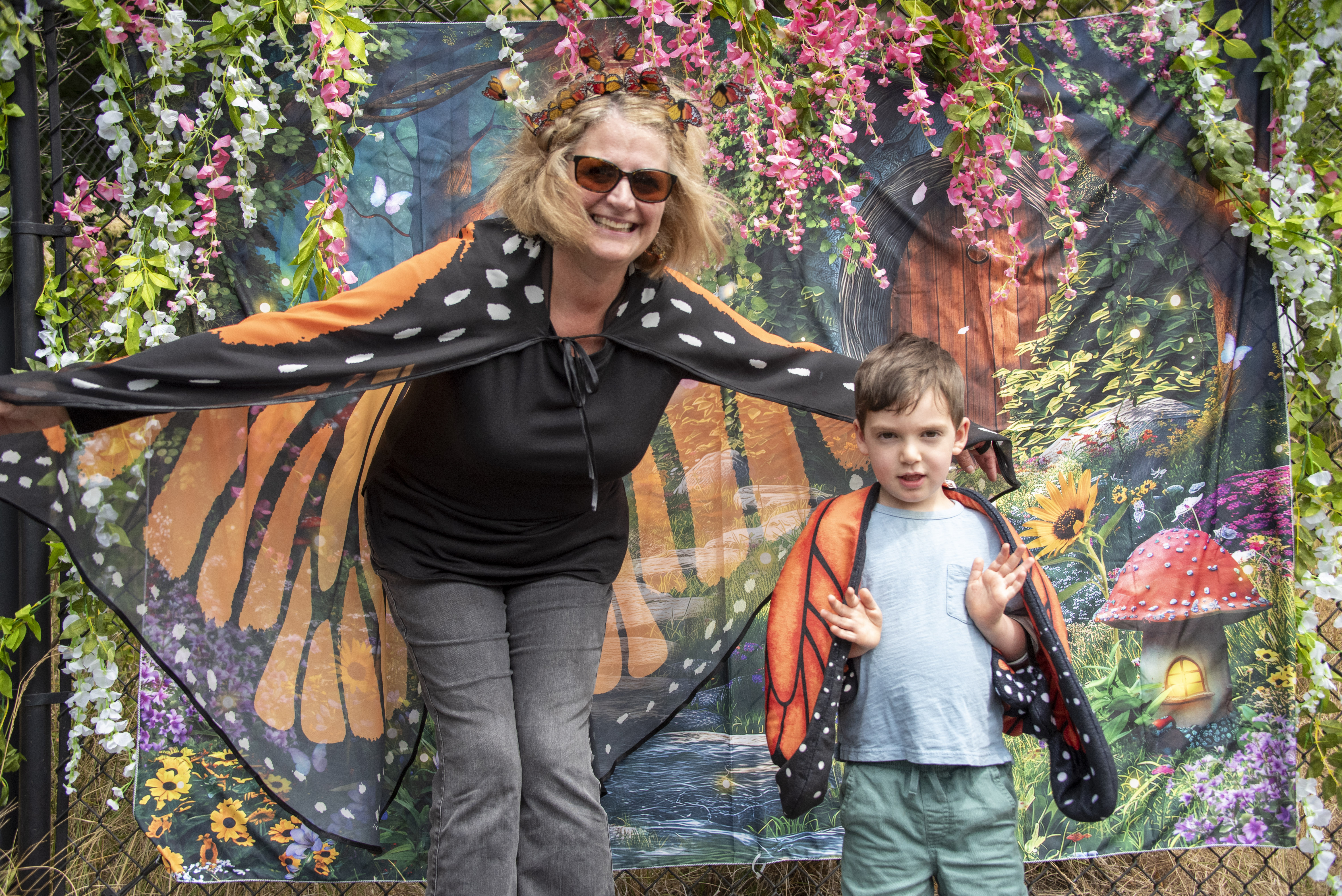 A woman in a butterfly cape spreads her arms next to a small boy in the same butterfly cape.