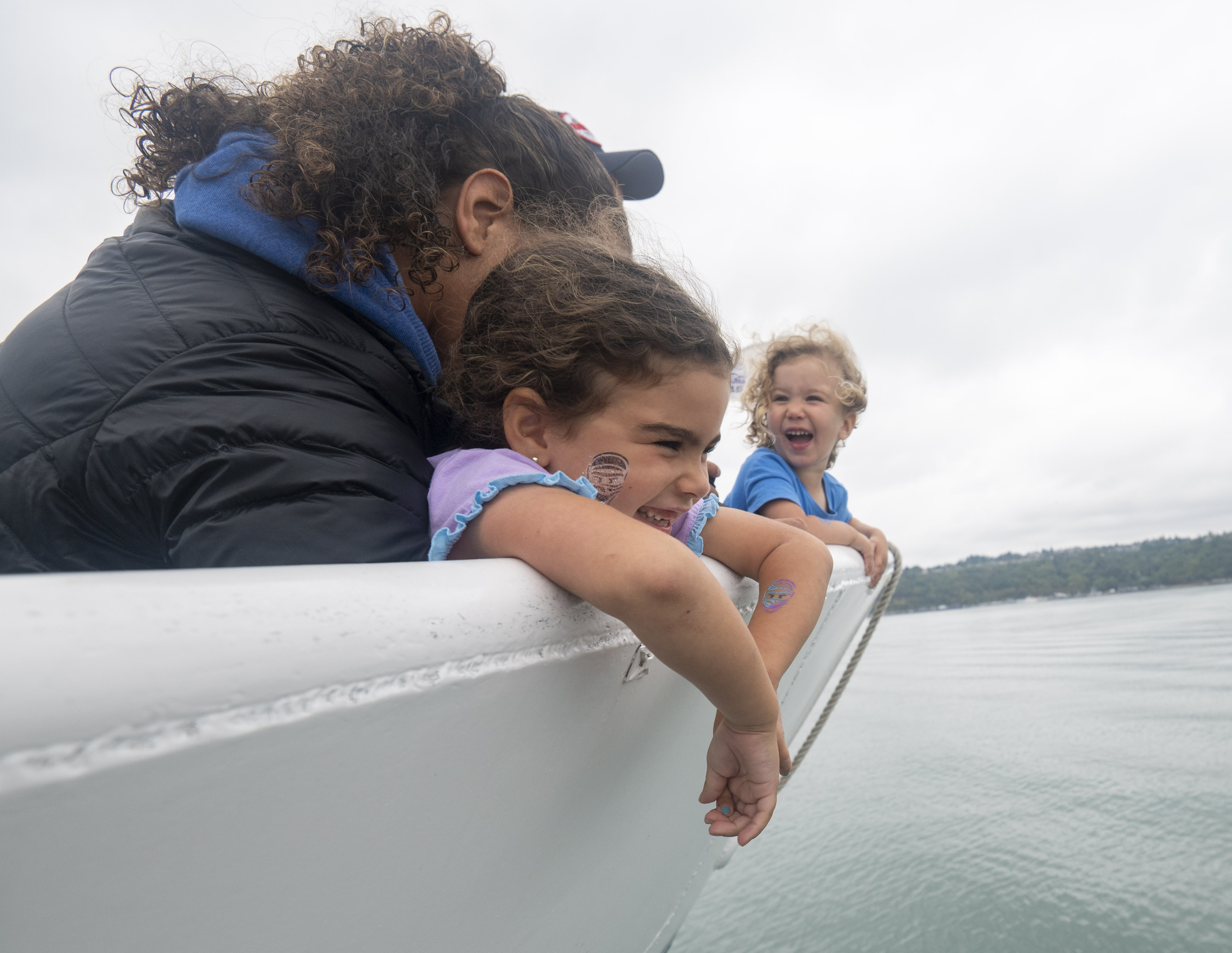 Two children lean on the edge of the boat, laughing, with their adult chaperone