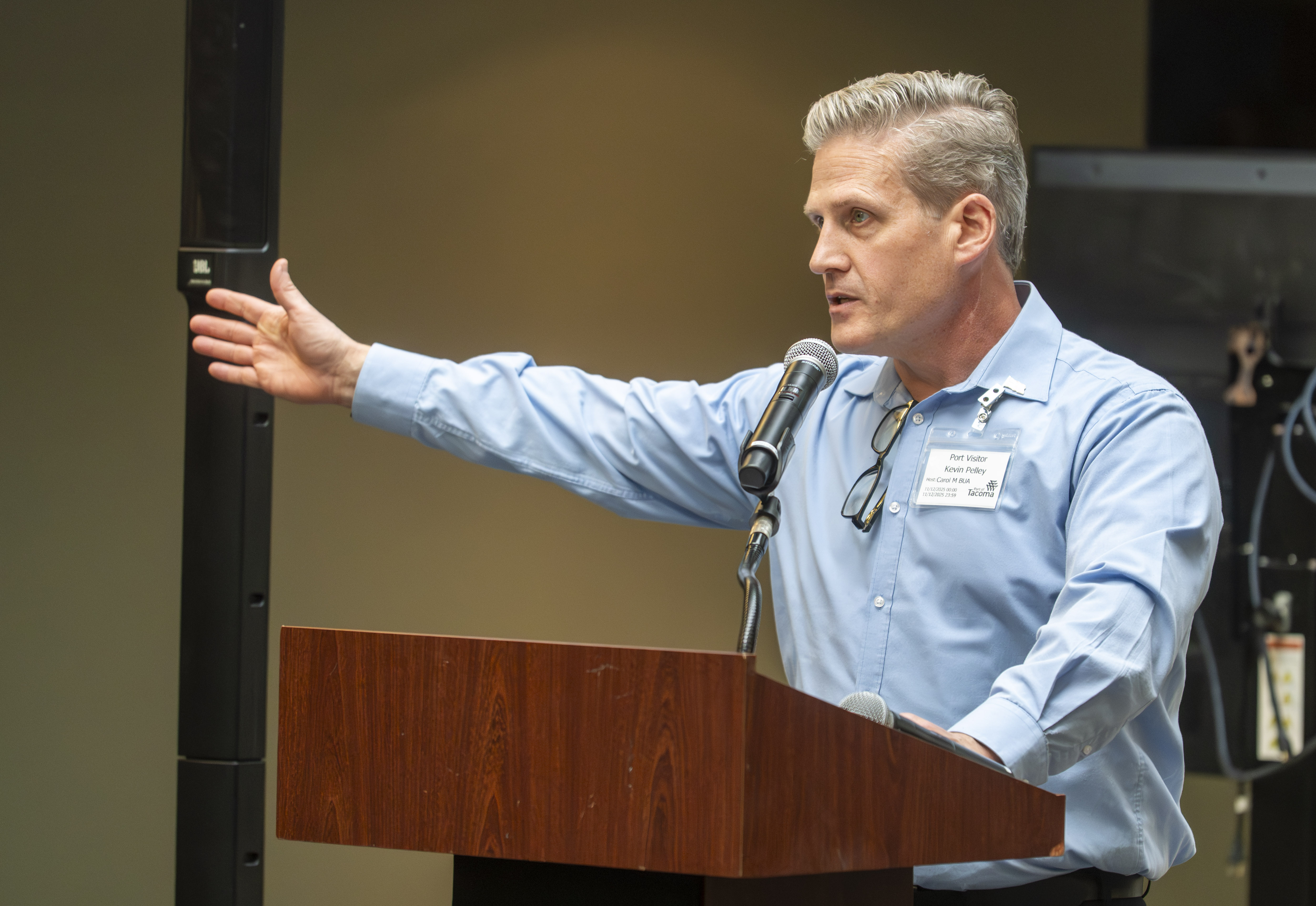 A man at a podium holds his arm out while speaking into a microphone. 