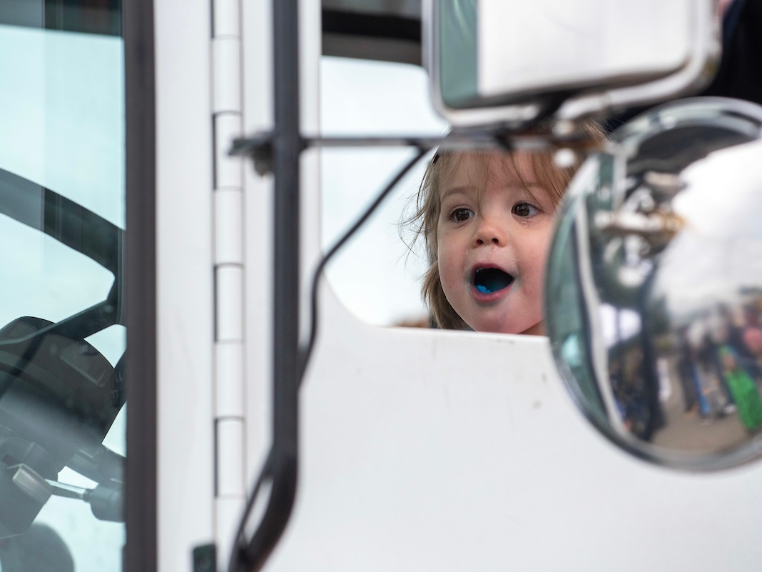 A toddler exclaims in excitement while sitting in the cab of a white truck.