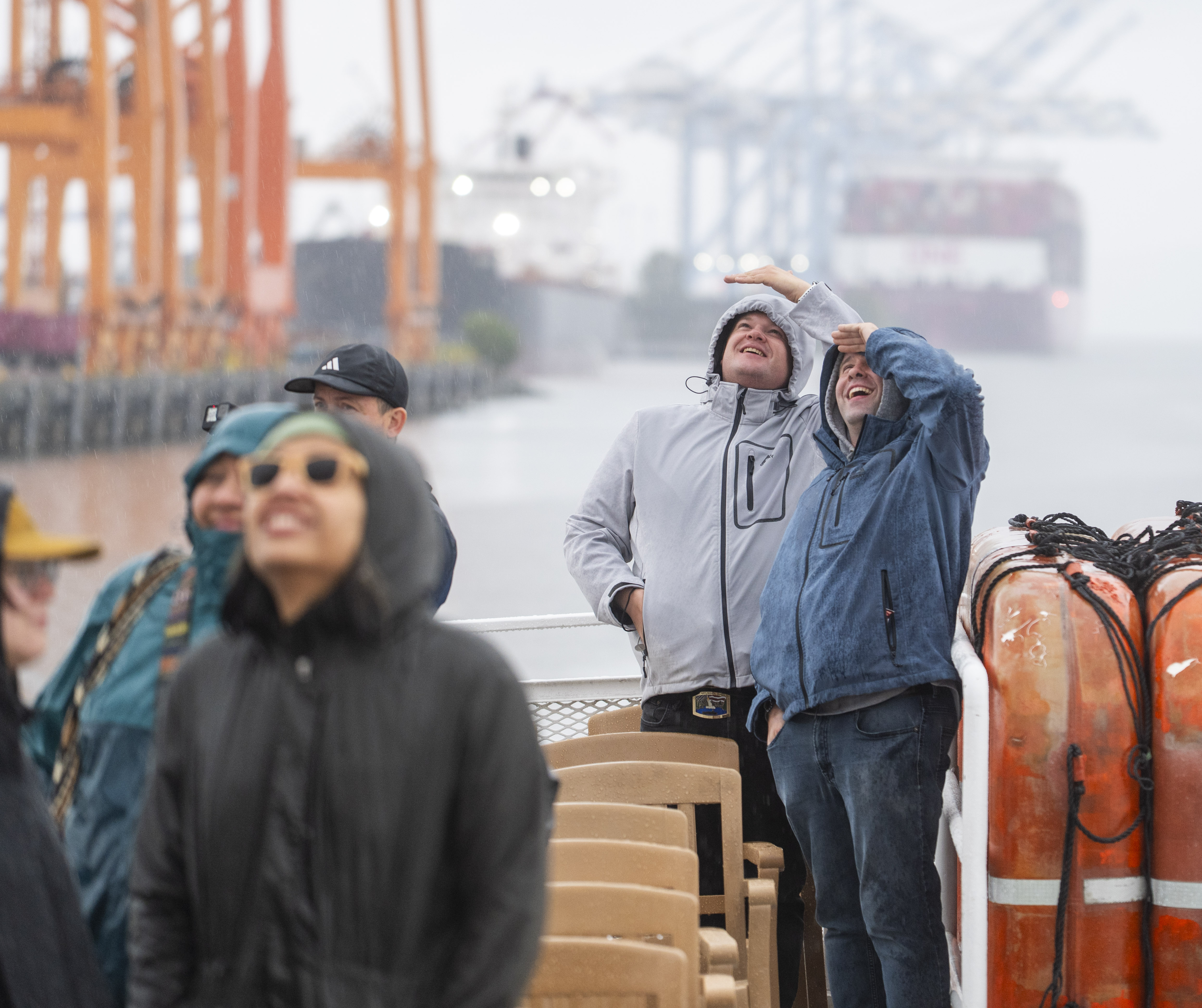 People taking a Port of Tacoma boat tour look up at a crane on a rainy day