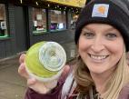 A woman in a black beanie smiles while holding up a round, lime green trinket