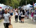 A man in a grey shirt walks through a group of booths at an outdoor event.