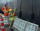 Two men in safety equipment pulling electrical cords down from a vessel.