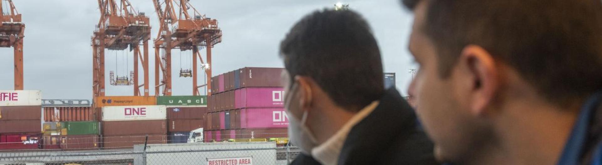 Two men looking out a bus window at some cranes. 